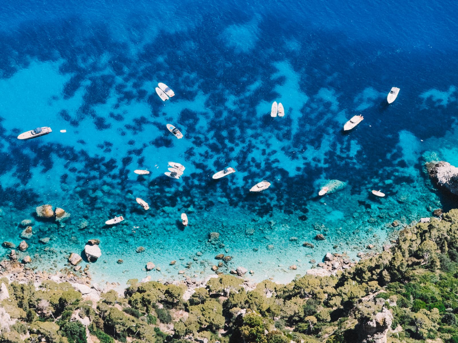 Boats swimming and anchoring in the clear turquoise waters around Capri