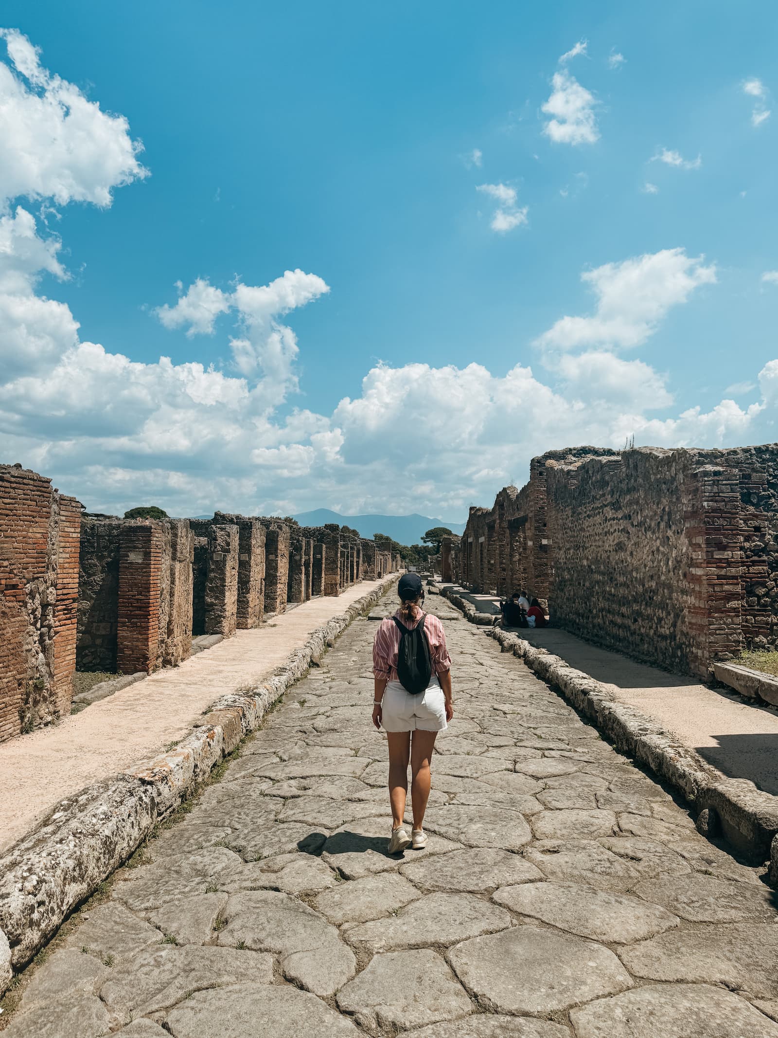 Woman standing in the middle of an ancient street in Pompeii with ruins on both sides.