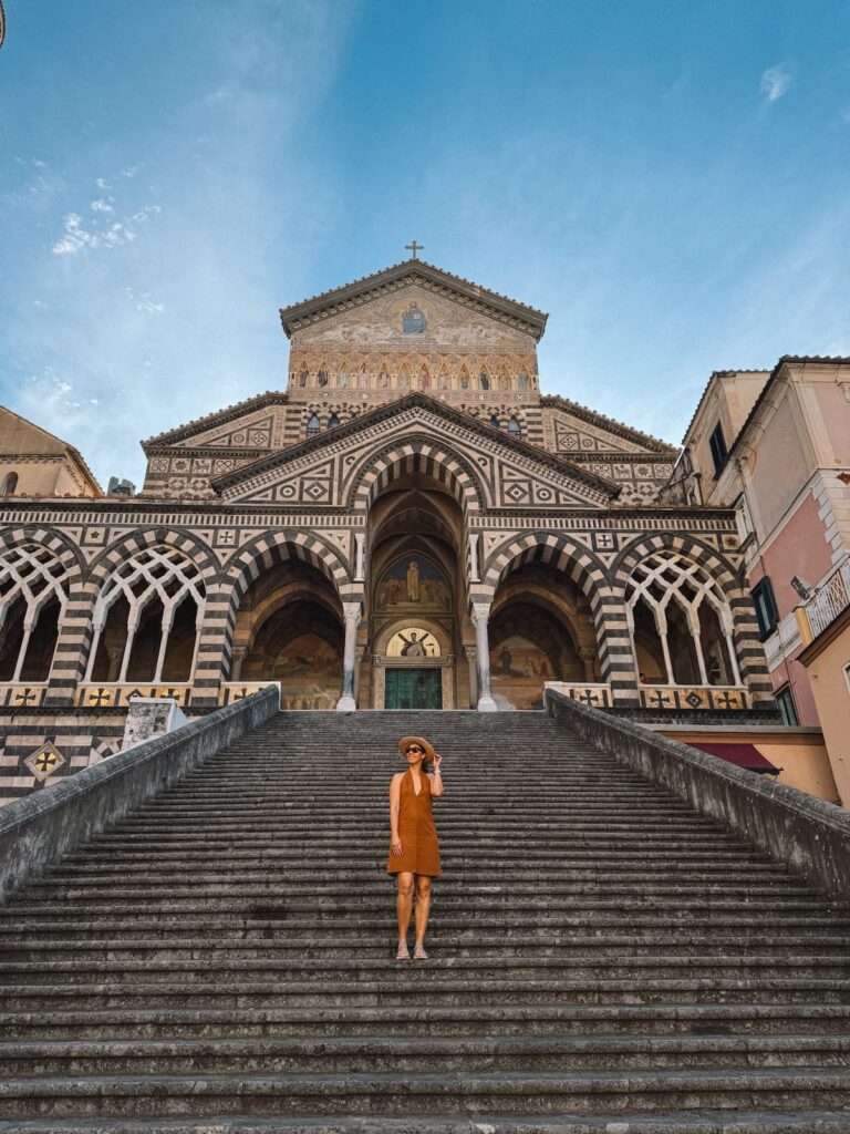 Woman with orange dress standing on the stairs in fronto of the Amalfi Duomo.