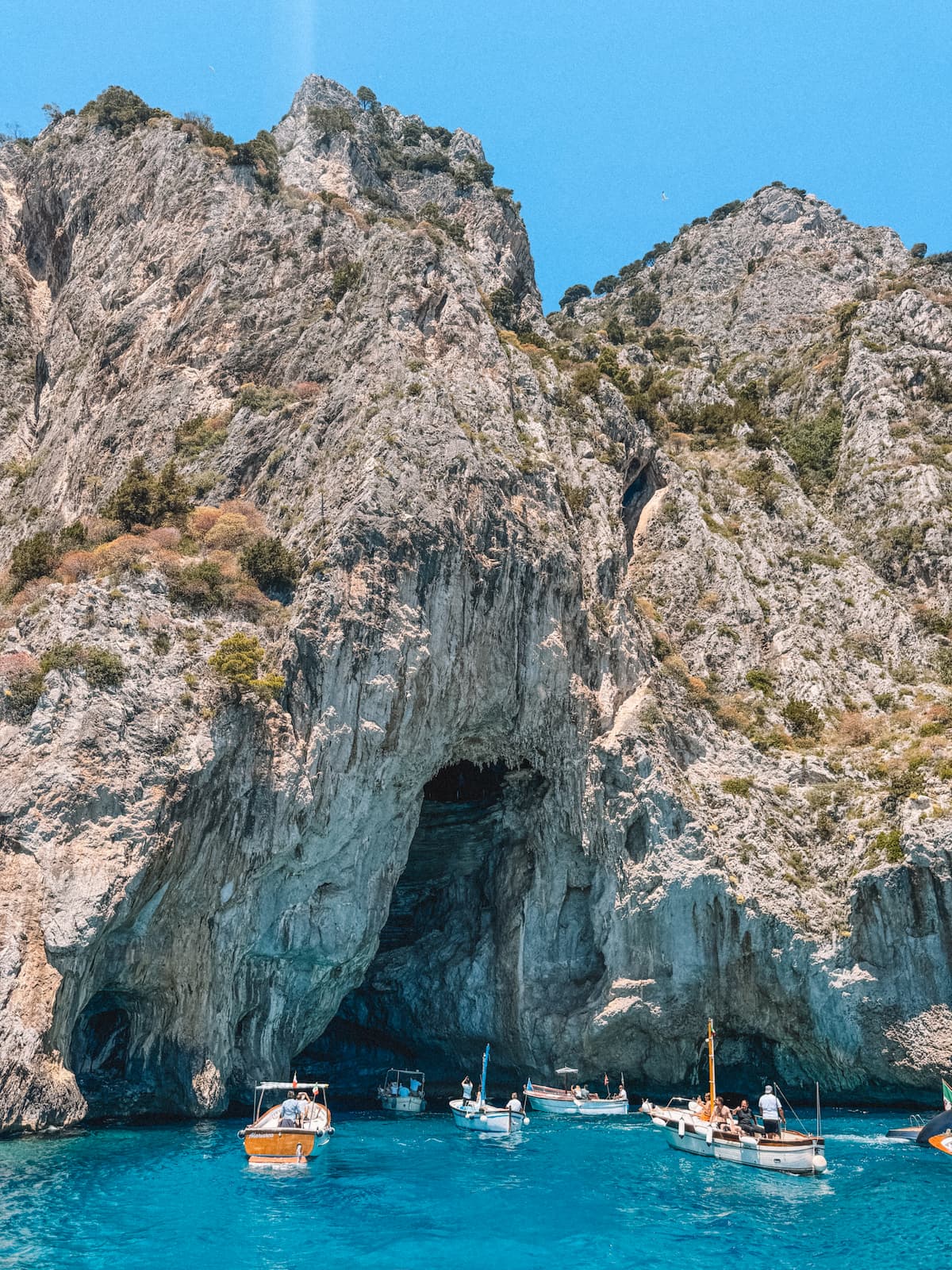 Small boats gathered near a sea cave on Capri with bright blue water and steep rocky cliffs