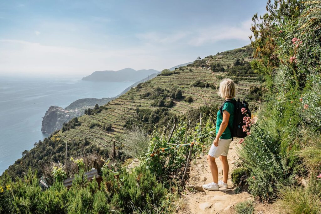 Woman hiking above the Cinque Terre coastline with sea views and terraced hills near Vernazza