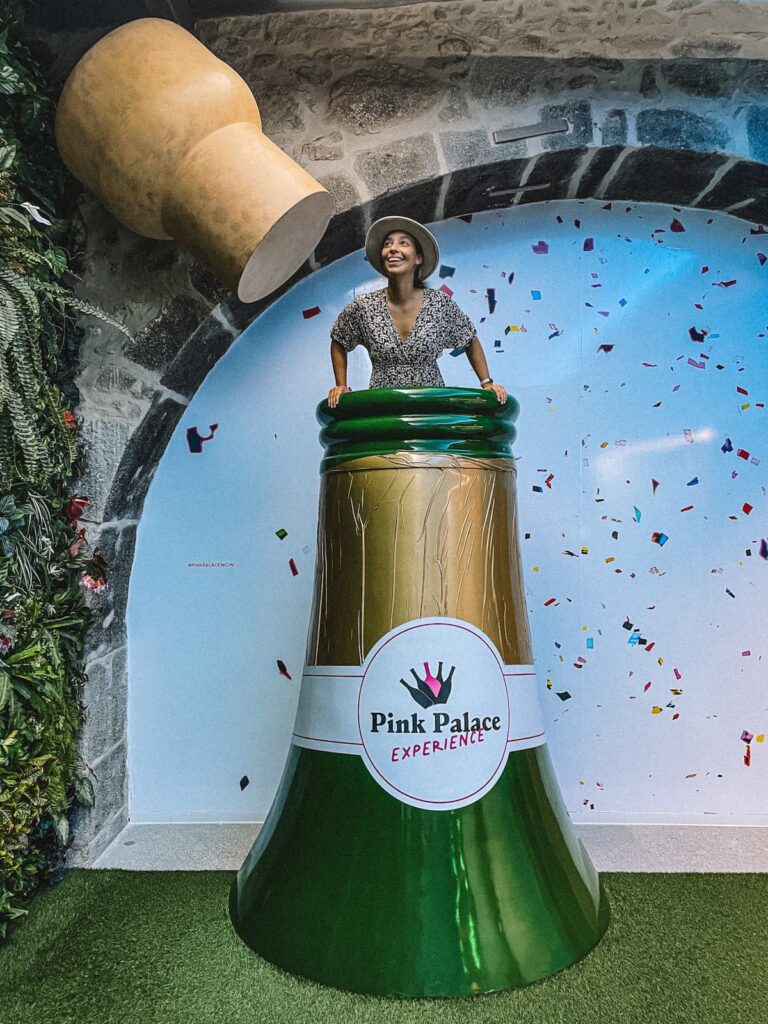 Woman posing inside a giant champagne bottle installation at Pink Palace wine museum in Porto