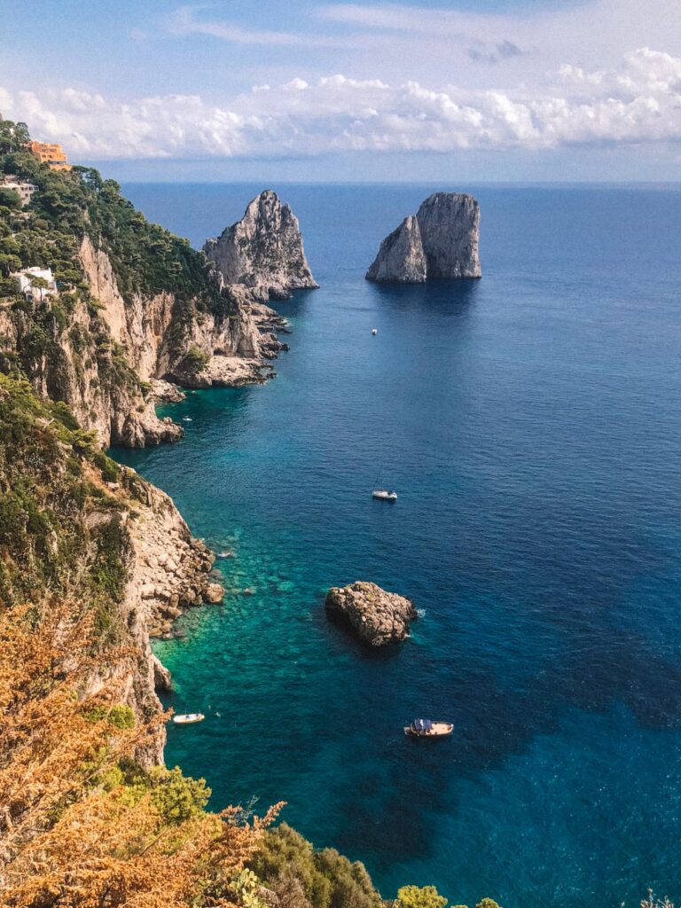 View of the Faraglioni sea stacks and Capri’s rocky coastline from above, with turquoise water and small boats below