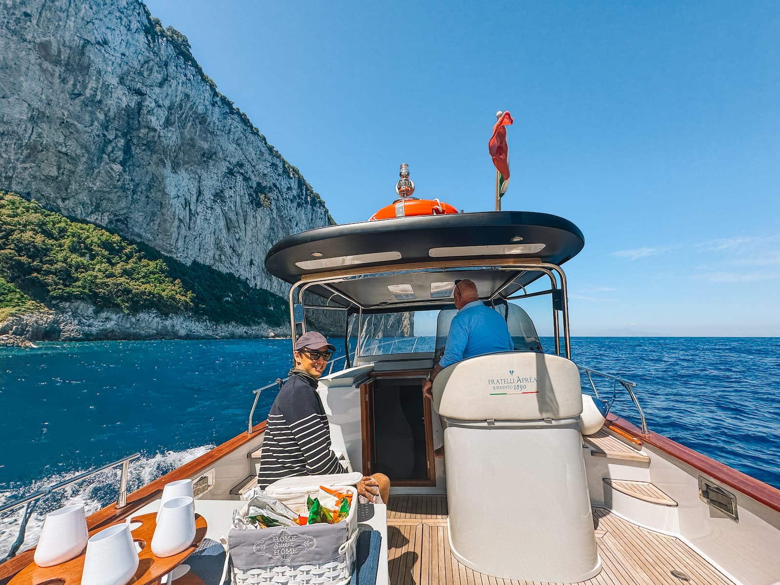 Boat tour around Capri, with passengers on board and steep rocky cliffs rising from the blue sea.