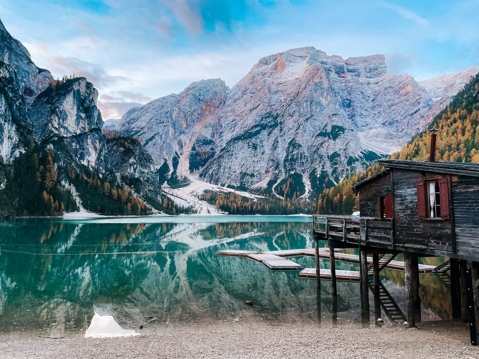 Lake Braies with turquoise water, wooden boat docks, a lakeside boathouse, and Dolomites peaks reflected in the water.