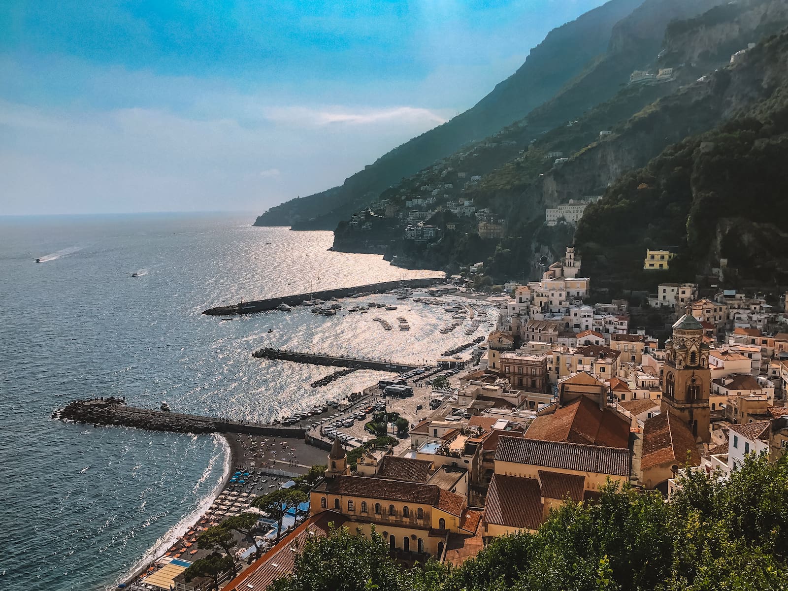 Scenic view of the Amalfi Coast with pastel-colored buildings, a harbor, cliffs, and the Mediterranean Sea.