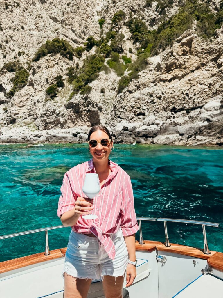 Woman holding a glass on a boat in the turquoise waters off the Polignano a Mare coast.