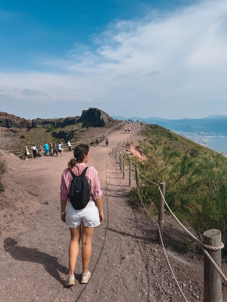 Woman hiking along the Mount Vesuvius crater trail with views over the Bay of Naples.