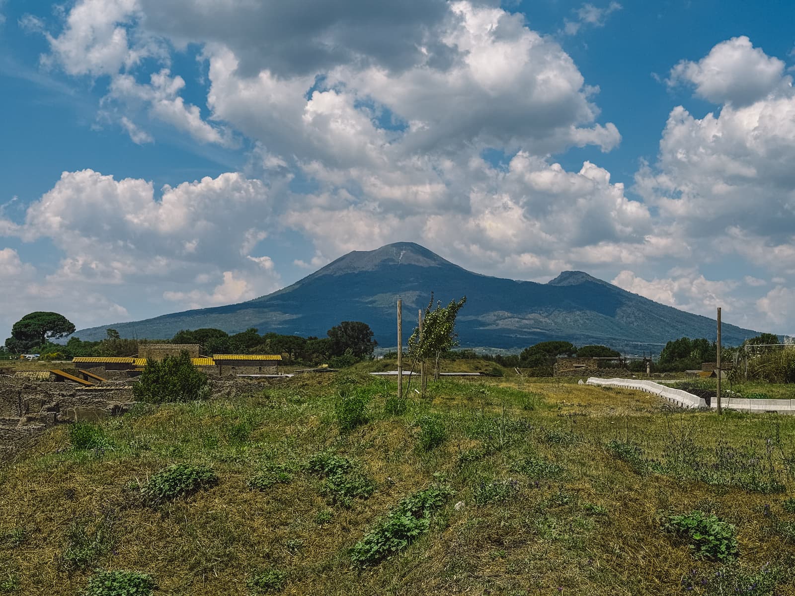Mount Vesuvius seen from Pompeii with ruins and green fields in the foreground.