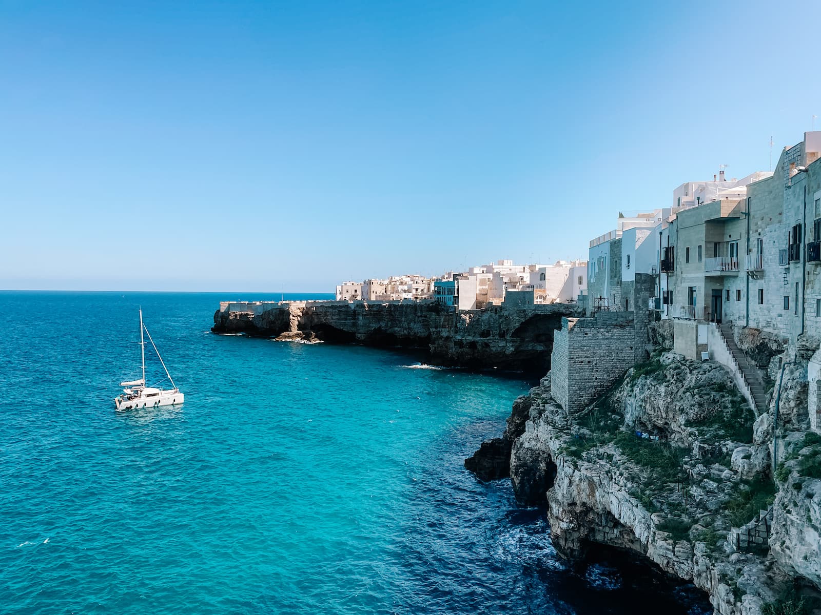 Catamaran sailing below the cliffs and whitewashed buildings of Polignano a Mare.