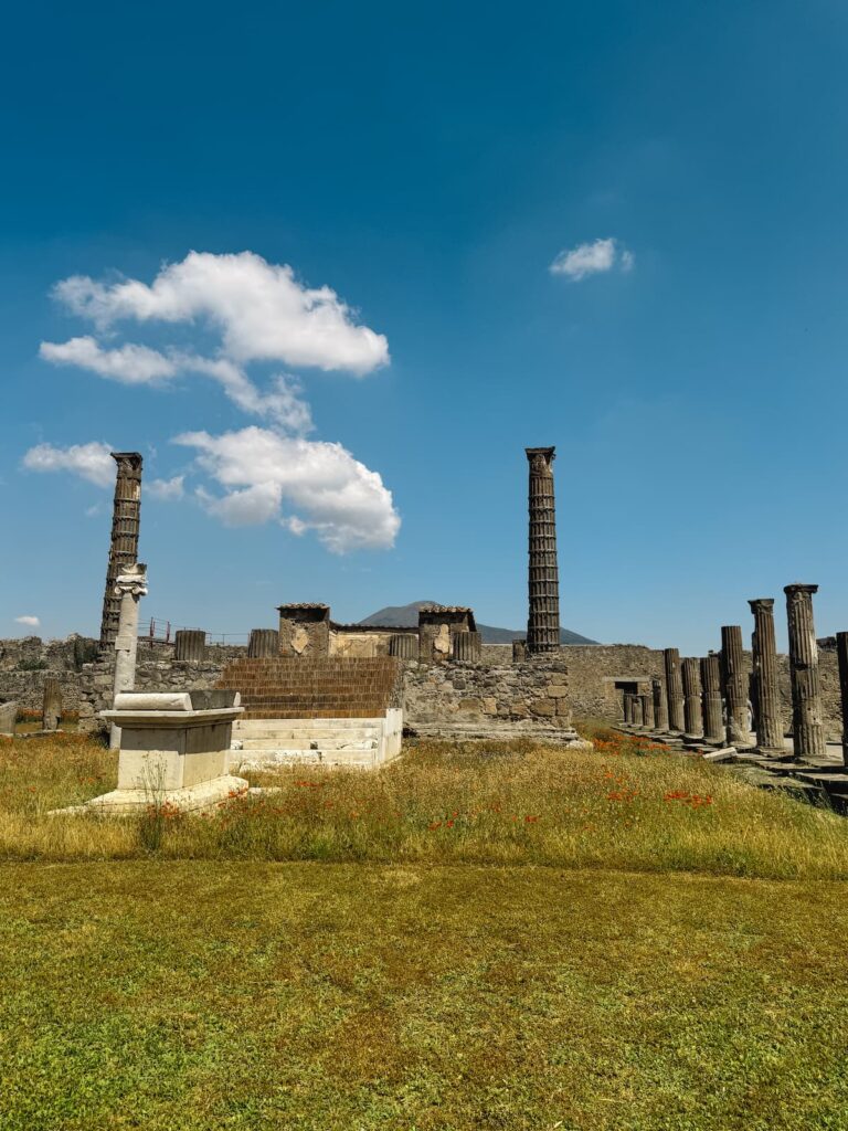 Pompeii ruins with Mount Vesuvius in the background under a blue sky.