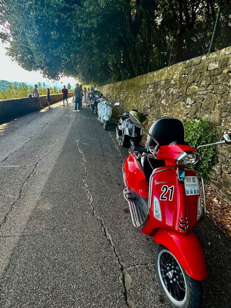 Red Vespa parked beside a stone wall on a road outside Florence.