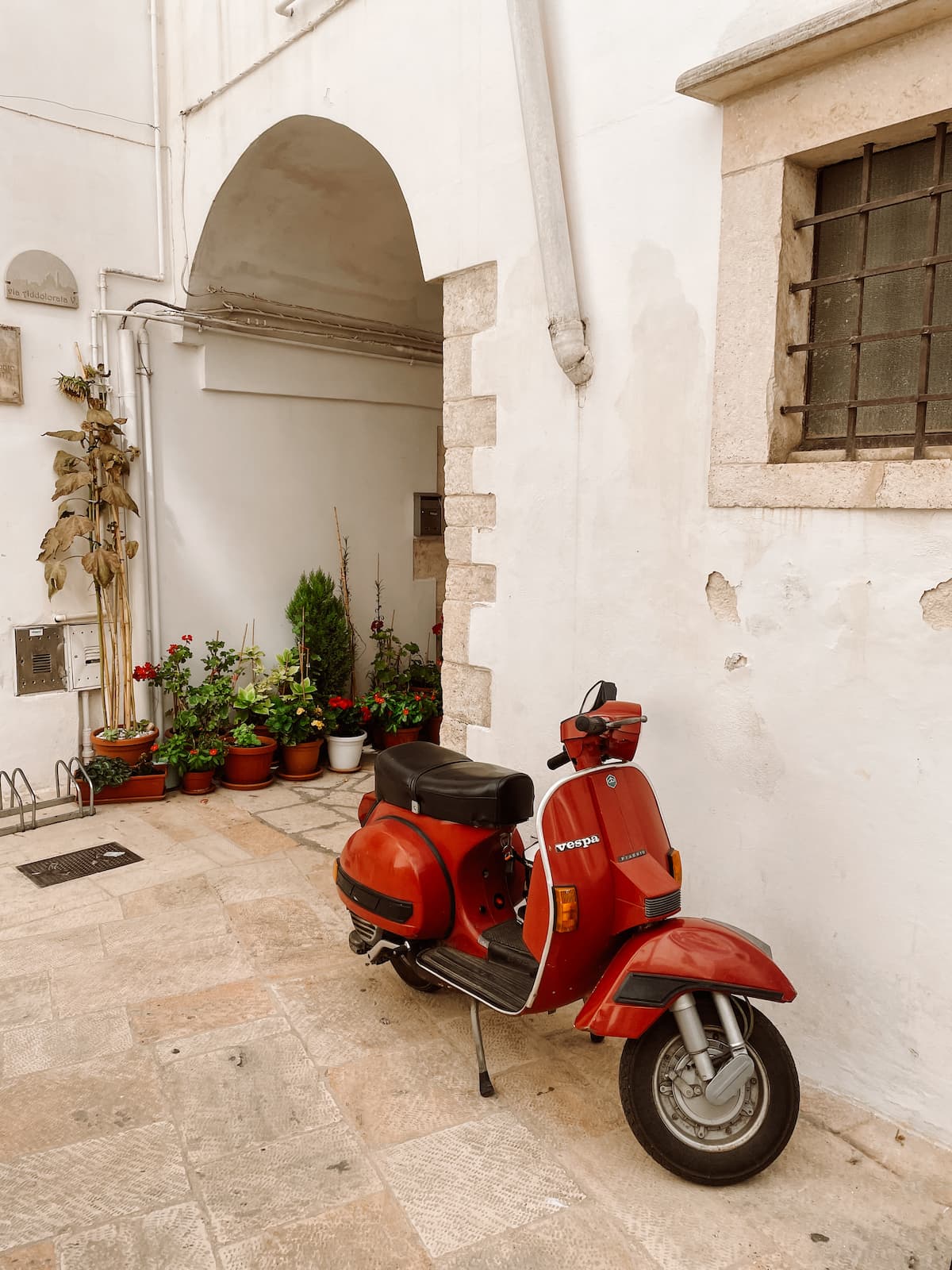 Red Vespa parked on a narrow whitewashed street in Italy.