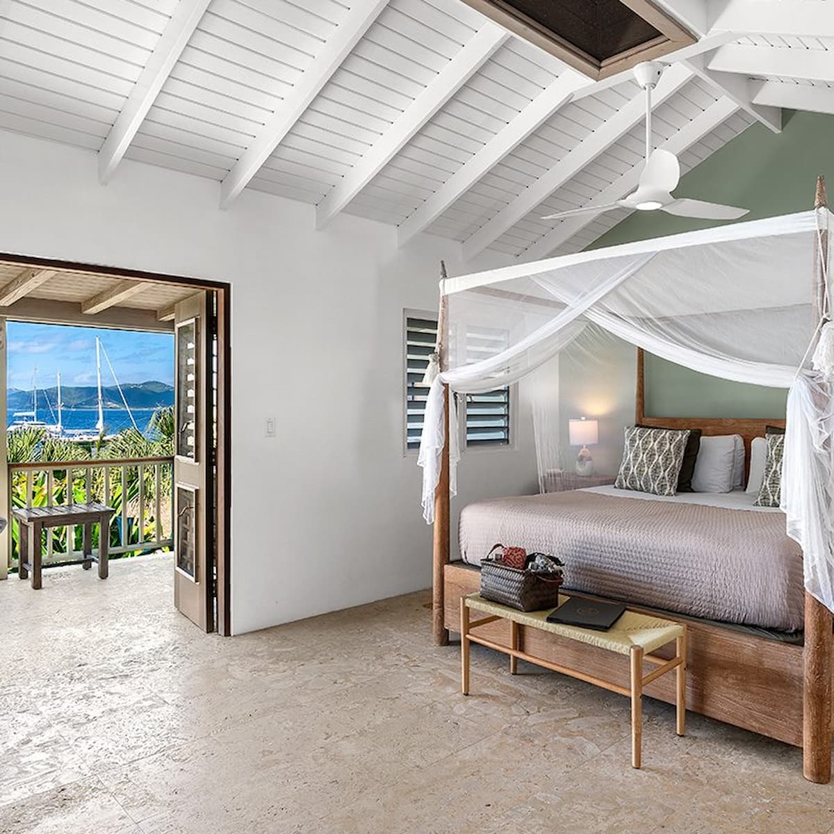 Bedroom with a canopy bed, ceiling fan, and sea-view balcony at Cooper Island Beach Club.