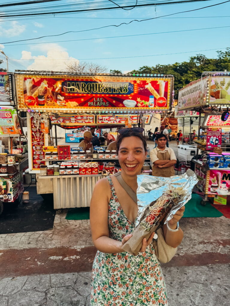 Stef holding a marquesita in front of a street-food stall in Cancun.