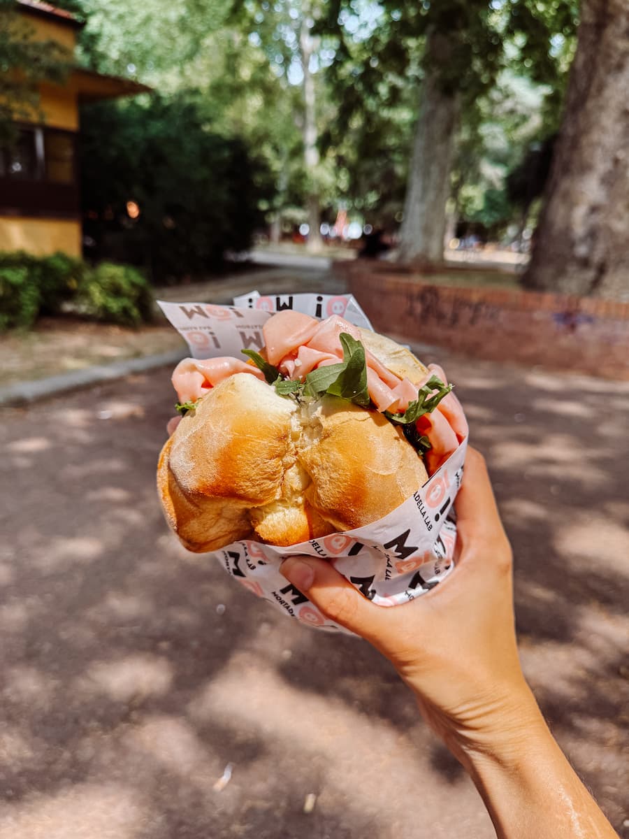 Hand holding a stuffed mortadella sandwich from Mò! Mortadella Lab in Bologna.