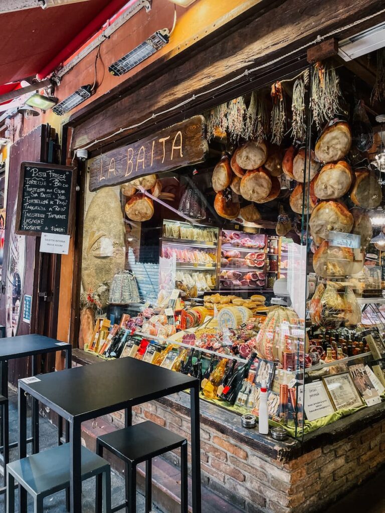 Food shop on Via Pescherie Vecchie displaying cured meats, cheeses, and other specialties.
