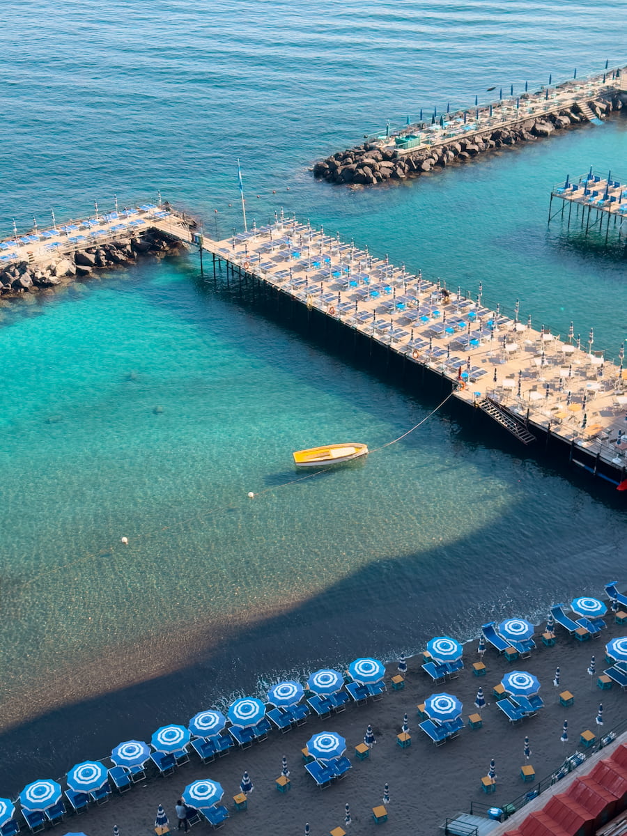 Sunbathing platforms, blue umbrellas, and clear water along Sorrento’s waterfront.